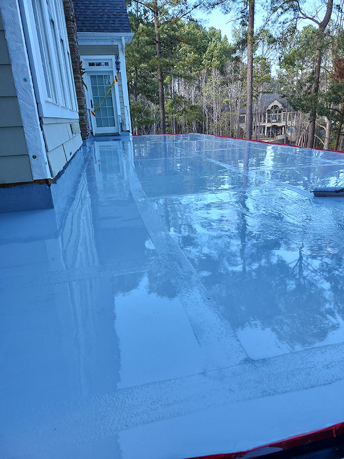 A shiny, freshly sealed flat deck outside a house, reflecting trees and surroundings.