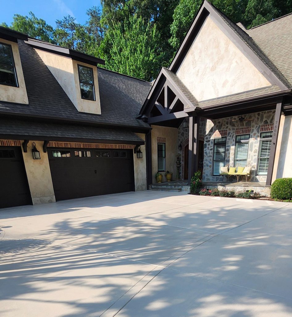 Modern house with three-car garage, stone accents, large windows, and tidy landscaping on a sunny day.