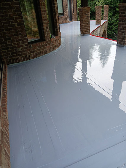 Shiny gray waterproof coating on a brick porch floor by a house with large windows and pillars.