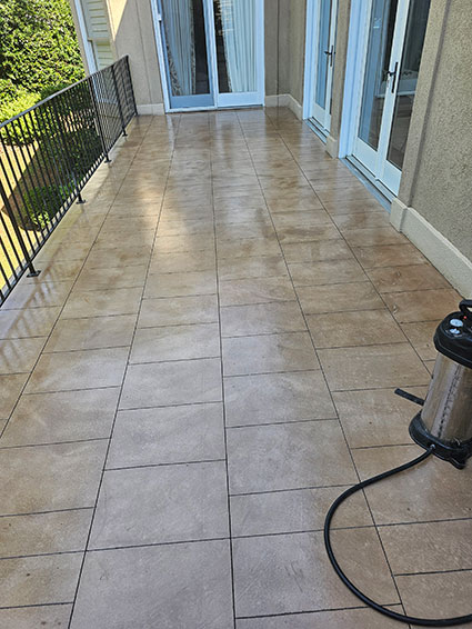 A clean tiled balcony with a railing, glass doors, and a floor cleaning machine on the right side.