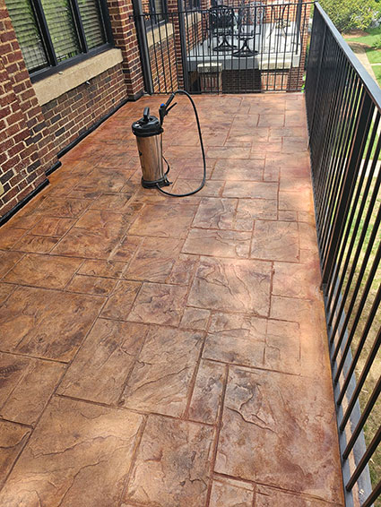 A stamped concrete balcony with a sprayer on top, surrounded by black metal railings.