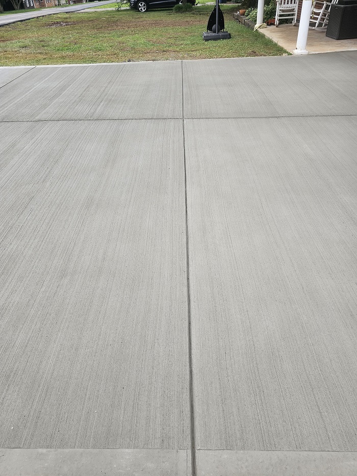 Freshly poured concrete driveway with visible brush lines and a control joint in the center.