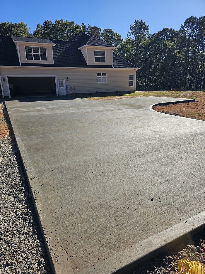 Freshly poured concrete driveway in front of a light-colored house with a double garage and green trees behind.