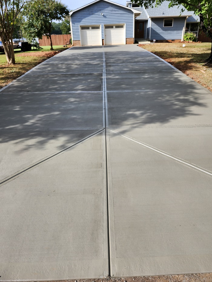 Freshly poured concrete driveway leading to a blue house with a two-car garage.