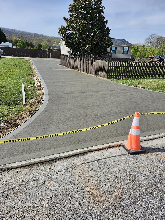 Freshly paved concrete driveway roped off with caution tape and a safety cone in front of a house.
