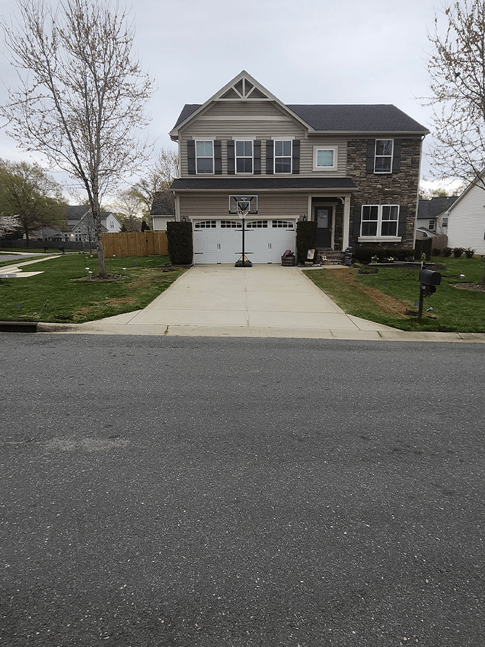 Two-story suburban house with a basketball hoop in the driveway, surrounded by trees and grass.
