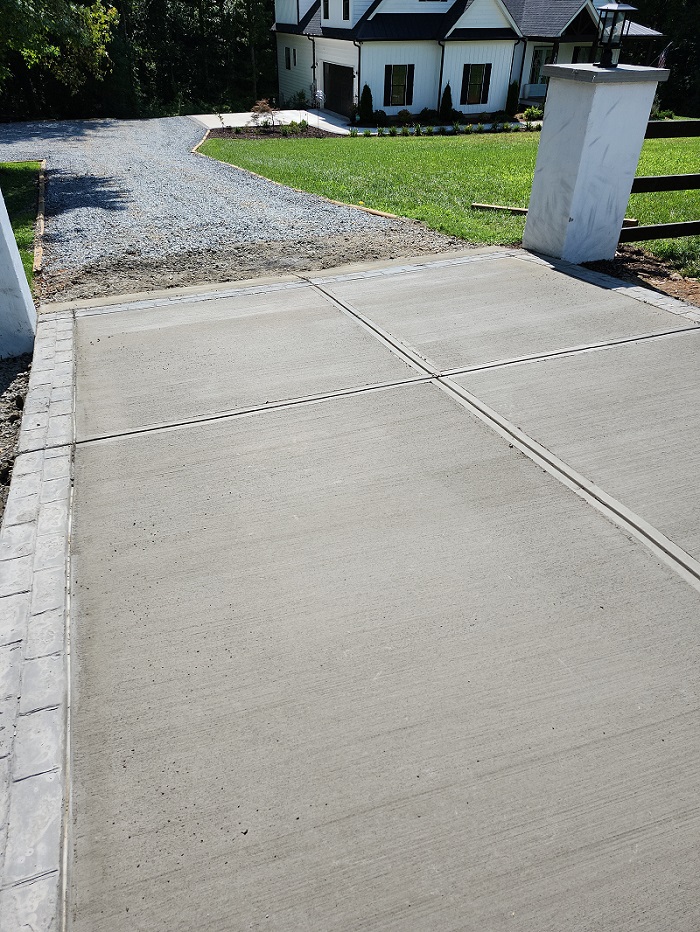 Freshly poured concrete driveway with a gravel path leading to a white house in the background.
