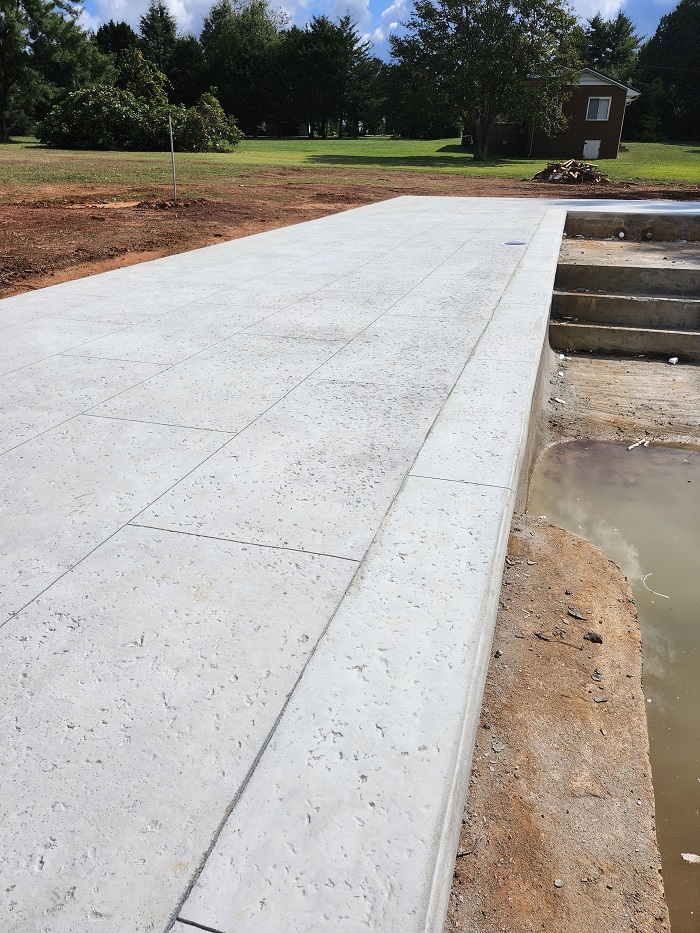 A newly poured concrete driveway with steps on the right and a grassy yard in the background.