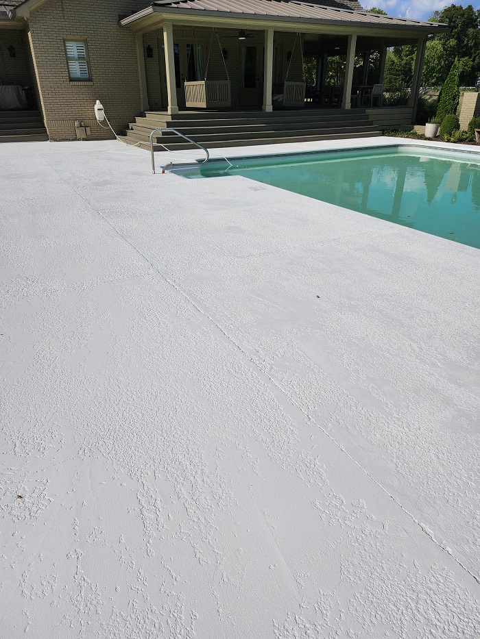 A house with a covered porch and steps leading to a pool with a textured, light-colored pool deck.