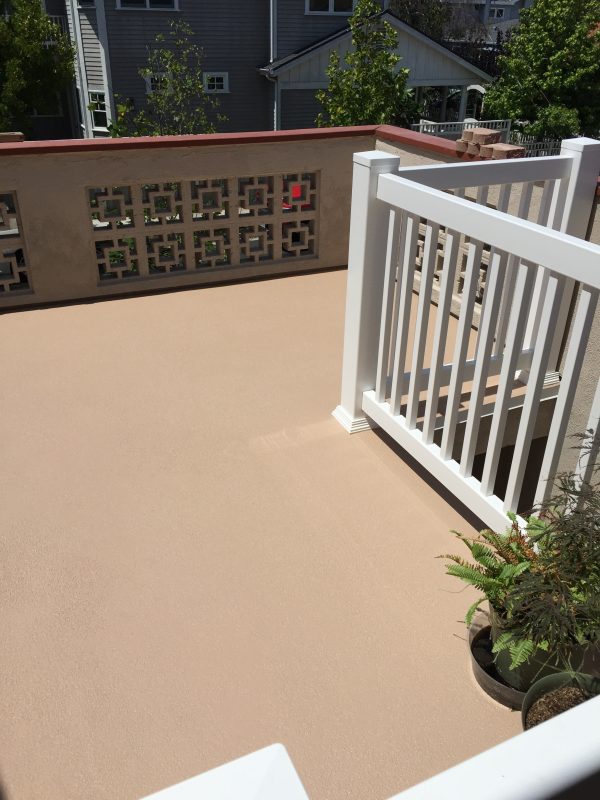 Sunny patio with tan flooring, white railings, potted plants, and decorative beige privacy wall panels.