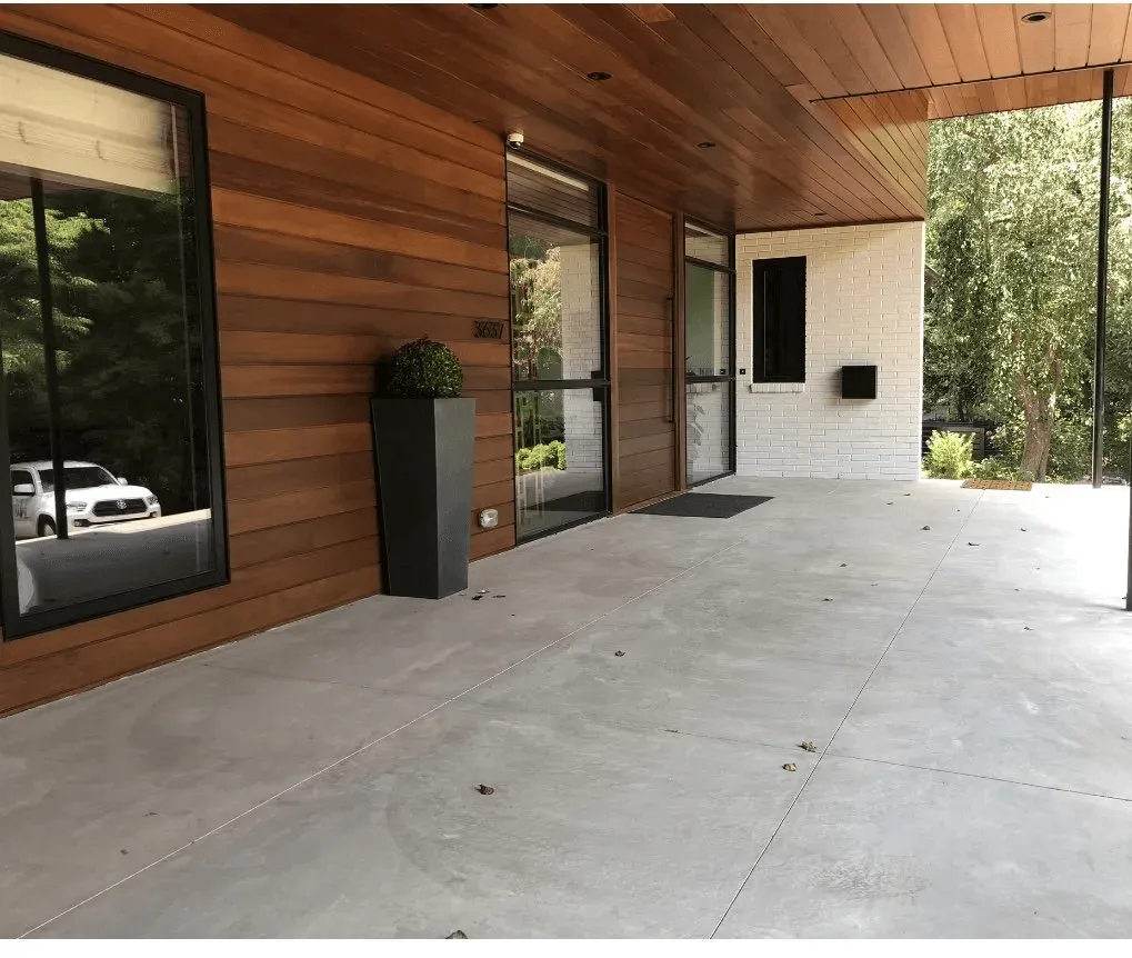 IMG_1803-201a0ba4-1920w-1280w Modern house entrance with wood siding, large windows, white brick, and a tall planter on a concrete porch.