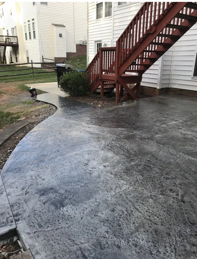 Concrete patio with a textured surface next to a red wooden staircase and a white house.
