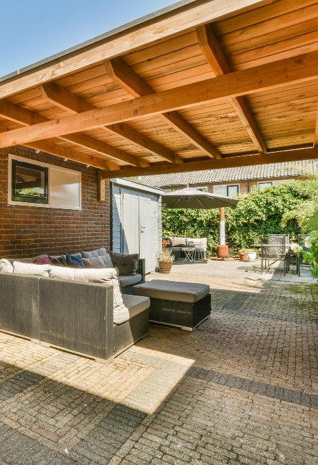 Covered patio with outdoor sofa, shed, and sunny courtyard with table, chairs, and umbrella.
