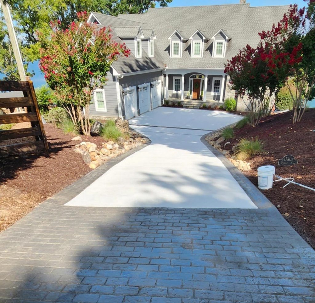A large house with a fresh concrete driveway, landscaping, and flowering trees on both sides.