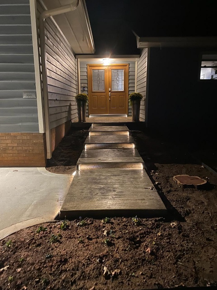 Concrete walkway with built-in lights leading to a double front door of a house at night.