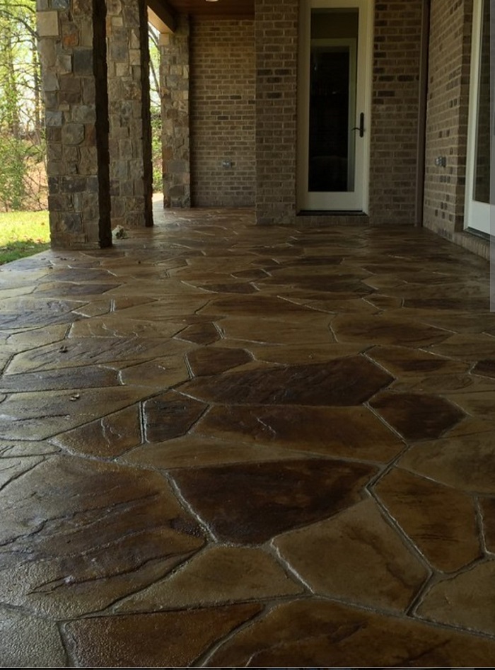 Brown stamped concrete patio with a stone pattern outside a brick house with large columns and a glass door.
