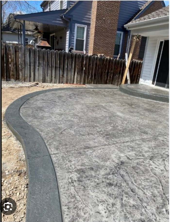 A backyard with a freshly poured and finished concrete patio near a wooden fence and house.