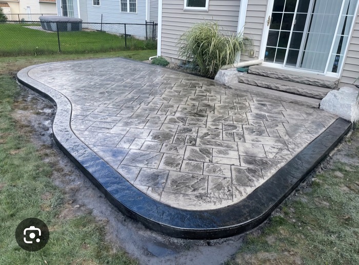 A newly installed stamped concrete patio with a curved edge beside a house and sliding glass door.
