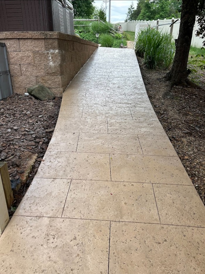 A smooth, tan concrete ramp slopes upward alongside a stone wall, bordered by rocks and greenery.