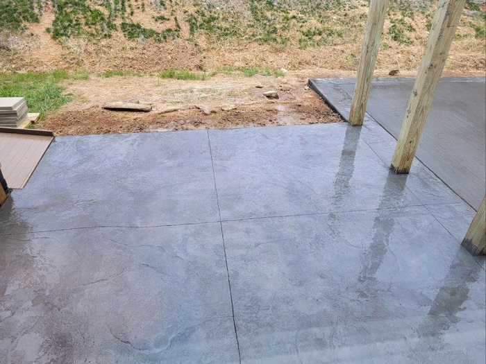 Wet concrete patio with wooden posts, bordered by grass and dirt in the background.