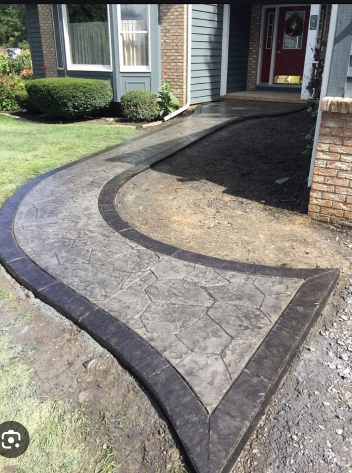 Curved stamped concrete walkway with dark borders leads to a house entrance with a red door.