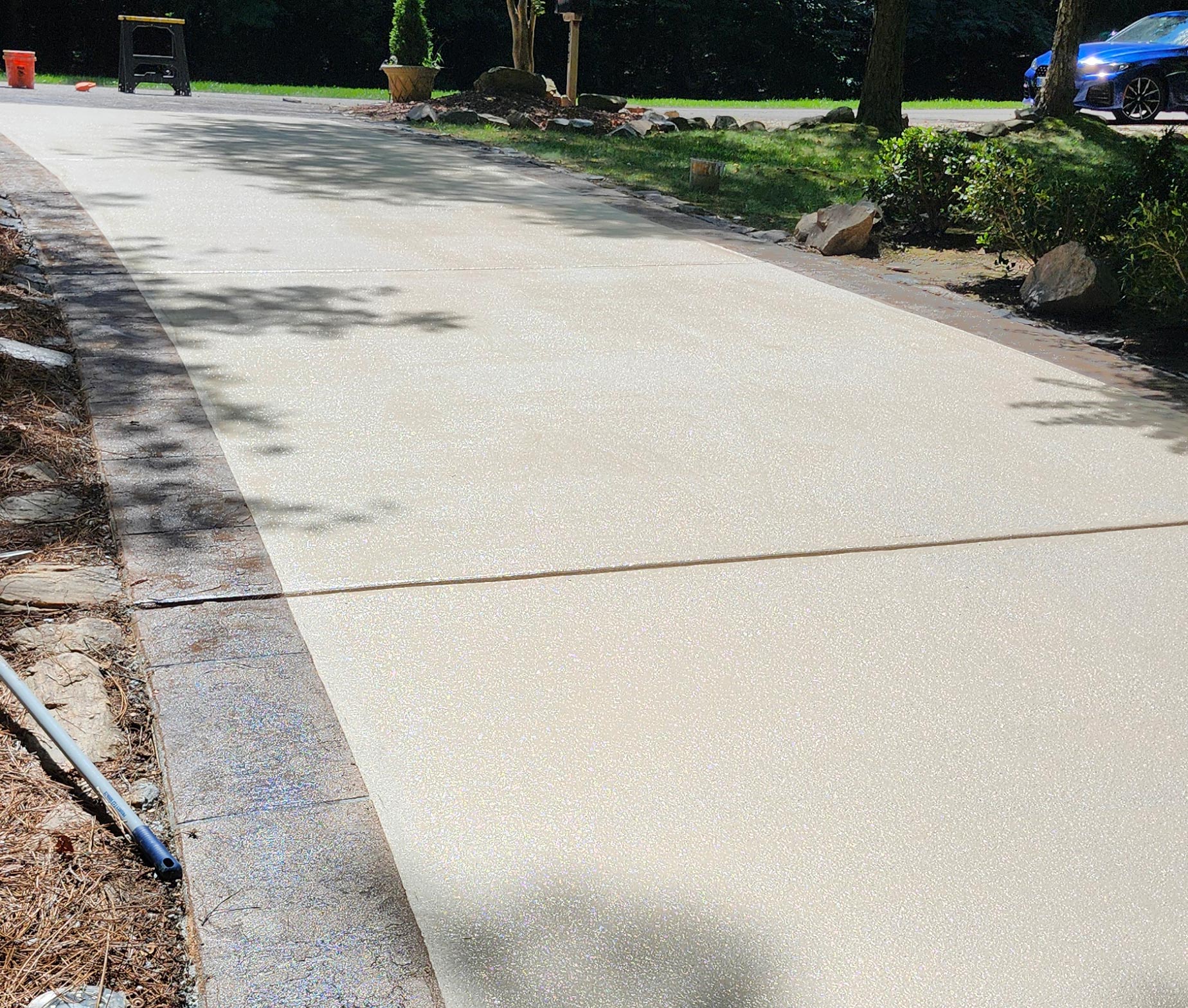 Freshly poured concrete driveway drying in sunlight, bordered by grass and landscaping.