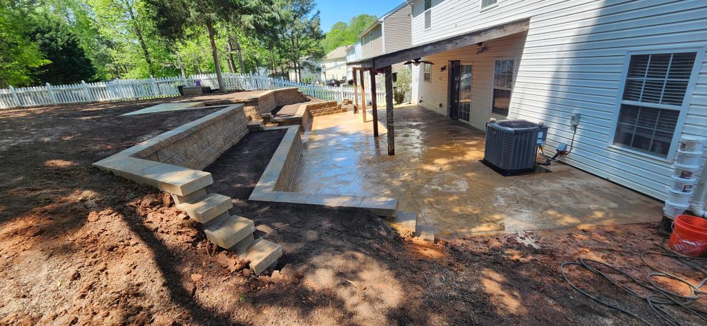 Backyard patio with stone steps, retaining walls, and a covered area attached to a white house.