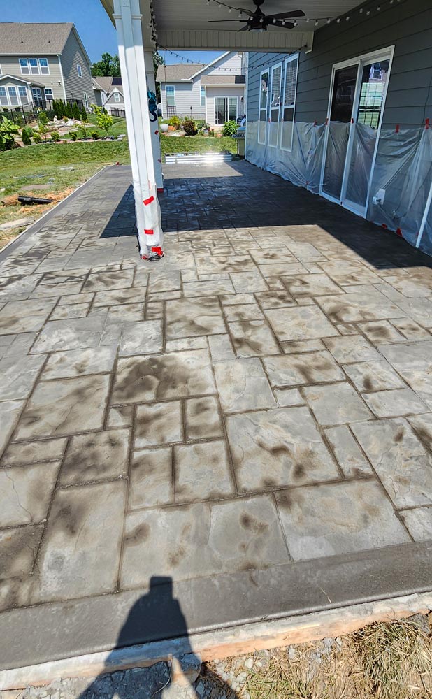 A newly stamped concrete patio with geometric patterns beside a house under a covered area.