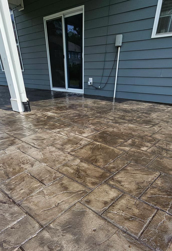 Brown stamped concrete patio with a geometric pattern outside a gray house with sliding glass doors.