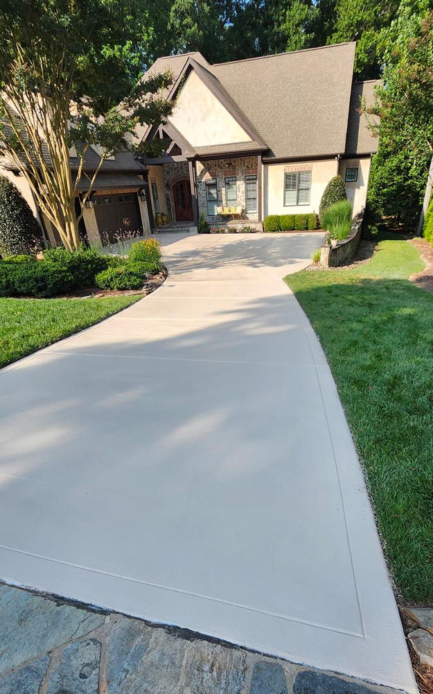 A freshly paved concrete driveway leads up to a suburban house with a landscaped front yard.