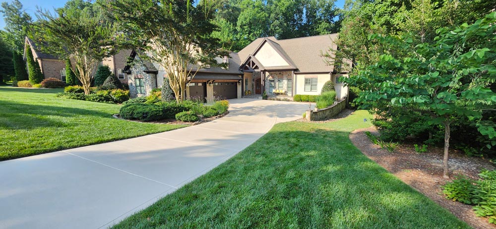 A modern house with a stone facade, three-car garage, and a curved driveway surrounded by green lawn and trees.