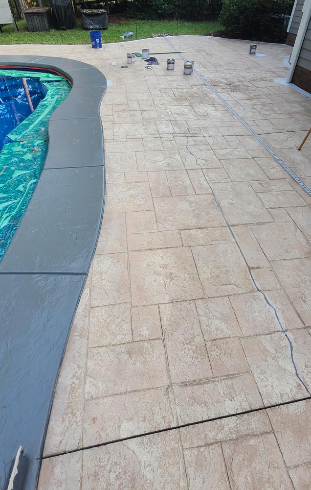 Stamped concrete pool deck with sealant cans and visible crack line running across the surface.