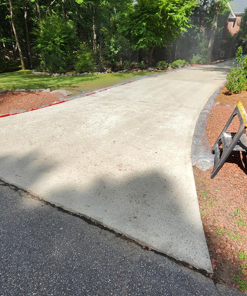 Freshly poured concrete driveway surrounded by red mulch and trees on a sunny day.