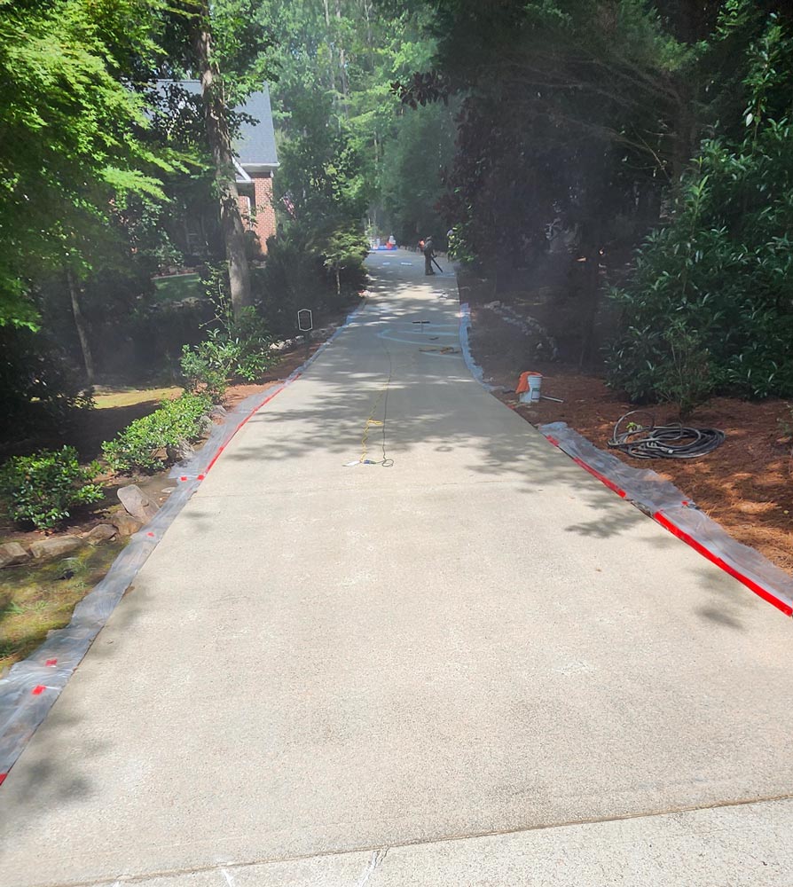A long driveway with fresh concrete surrounded by trees and landscaping on a sunny day.
