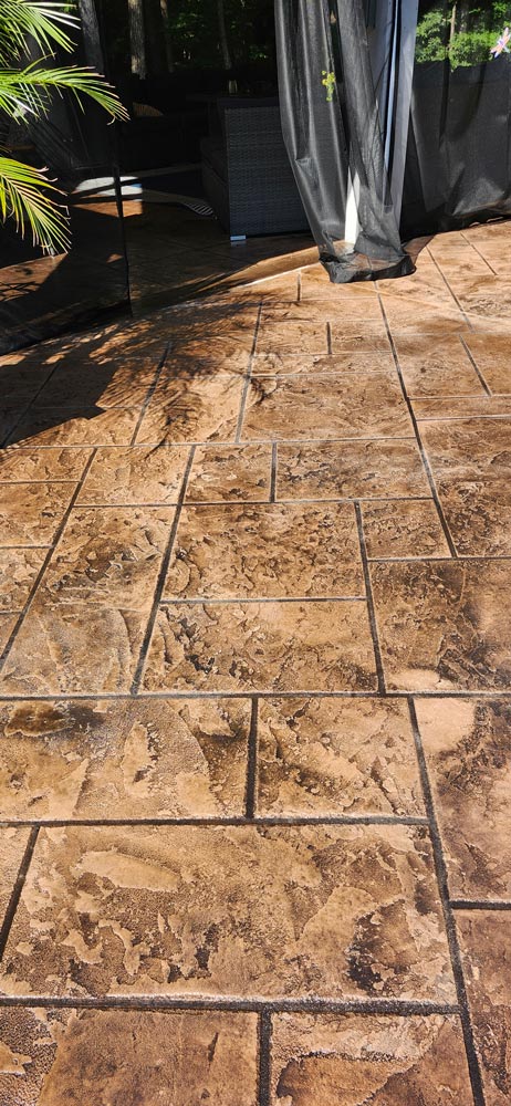 Stamped brown stone patio with sunlight and shadows, near black mesh curtains and outdoor furniture.