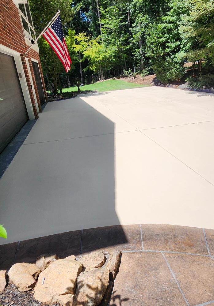 A clean, light-colored driveway leads to a garage with an American flag, bordered by green trees.