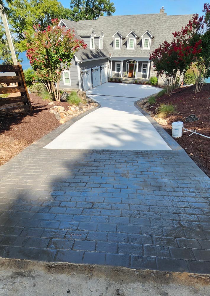A house with a driveway featuring dark stamped concrete leading to smooth white concrete near the garage.