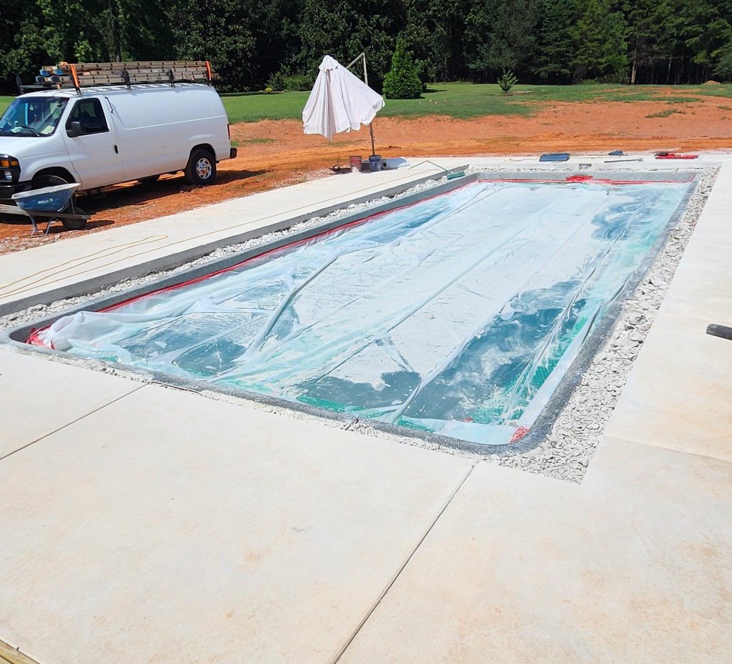 A rectangular in-ground pool under construction, covered with plastic, next to a white van and umbrella.