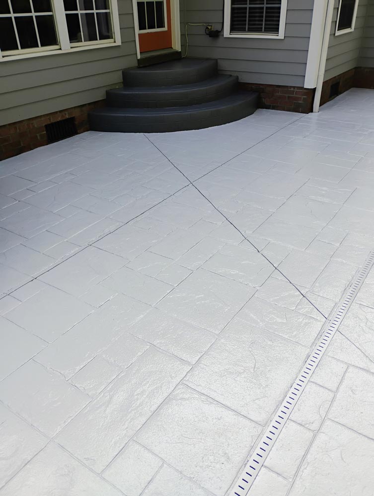 A newly painted white patio with a stamped stone pattern in front of gray house steps and an orange door.