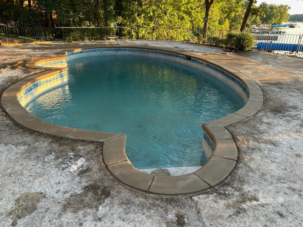 Heart-shaped swimming pool with clear water, surrounded by rough concrete and trees in the background.