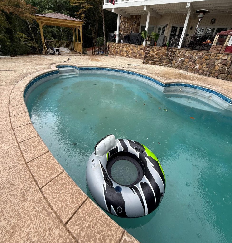 Black and white inflatable pool float in a backyard swimming pool on a rainy day.