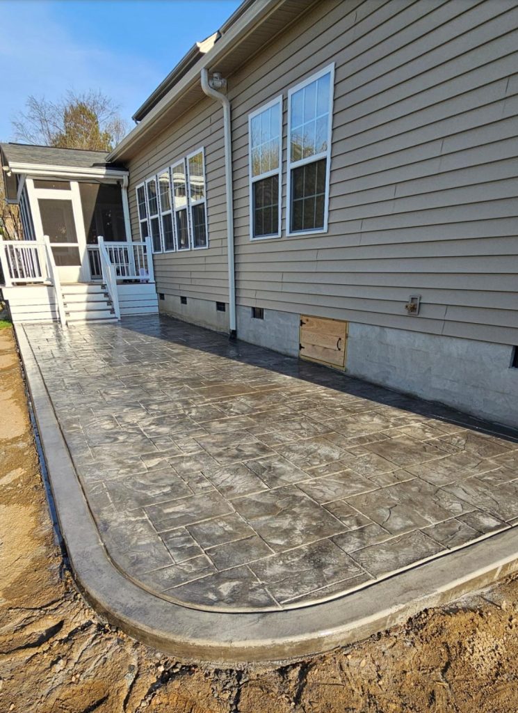 Stamped concrete patio with a border, next to a beige house and white steps leading to a porch.