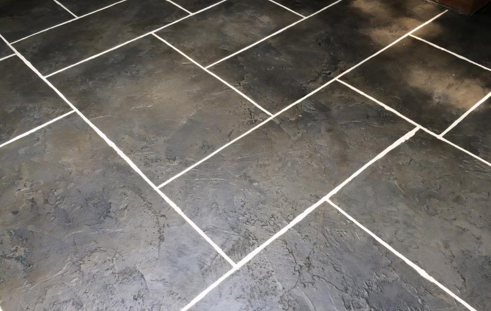 Close-up of dark, textured floor tiles with wide, white grout lines arranged in a staggered pattern.
