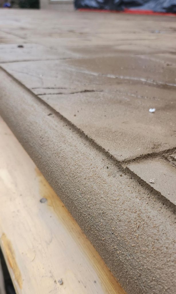 Close-up of a freshly poured concrete edge with a smooth finish on a wooden surface.