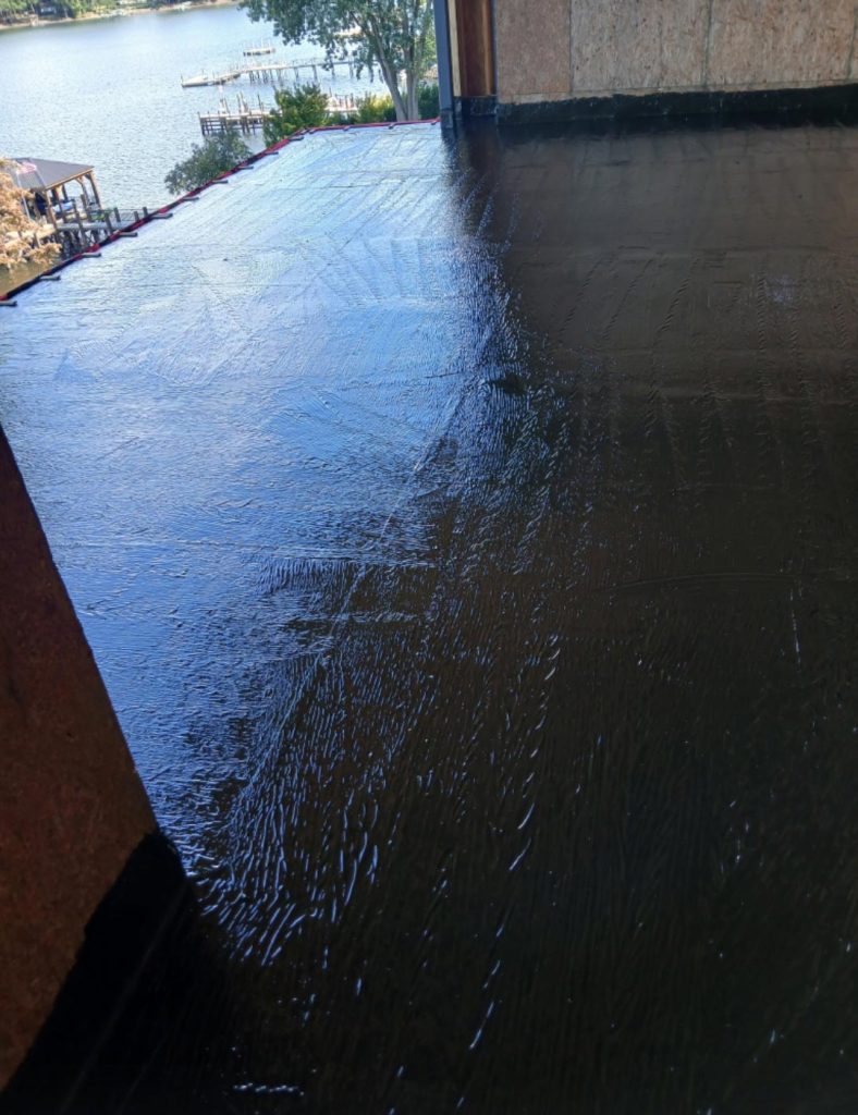 A freshly coated, wet black floor inside a building with a lake and docks visible outside.