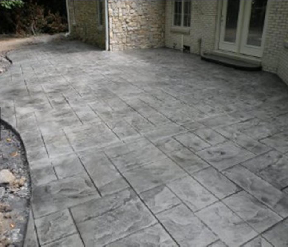 Gray stamped concrete patio with a rectangular pattern next to a brick house and glass doors.