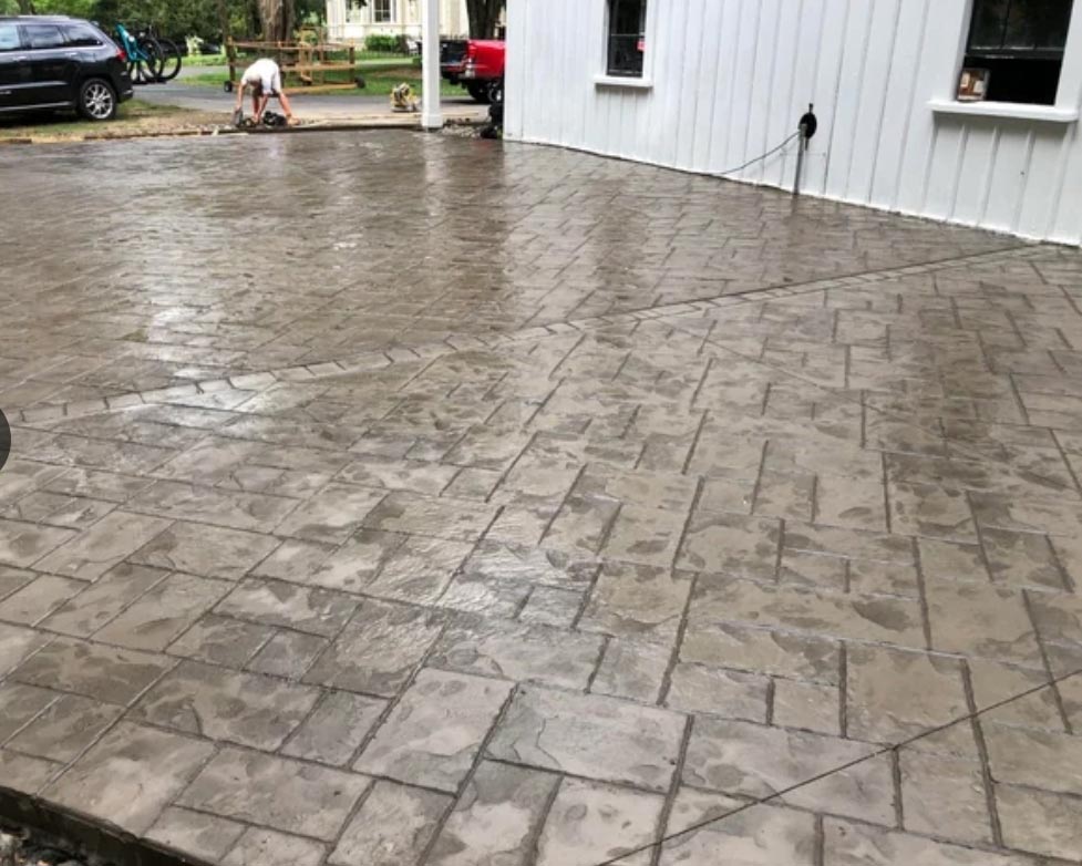 Freshly poured and stamped concrete patio with a brick pattern outside a white building.