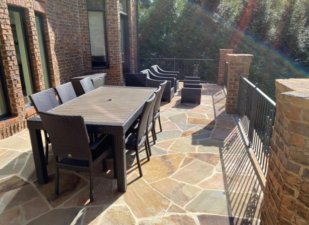 Outdoor patio with a dining table, chairs, lounge seats, and stone flooring in sunlight.