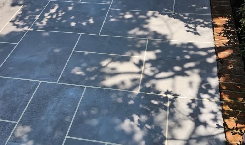 Shadows of tree branches cast on large gray stone tiles next to a brick edge in sunlight.