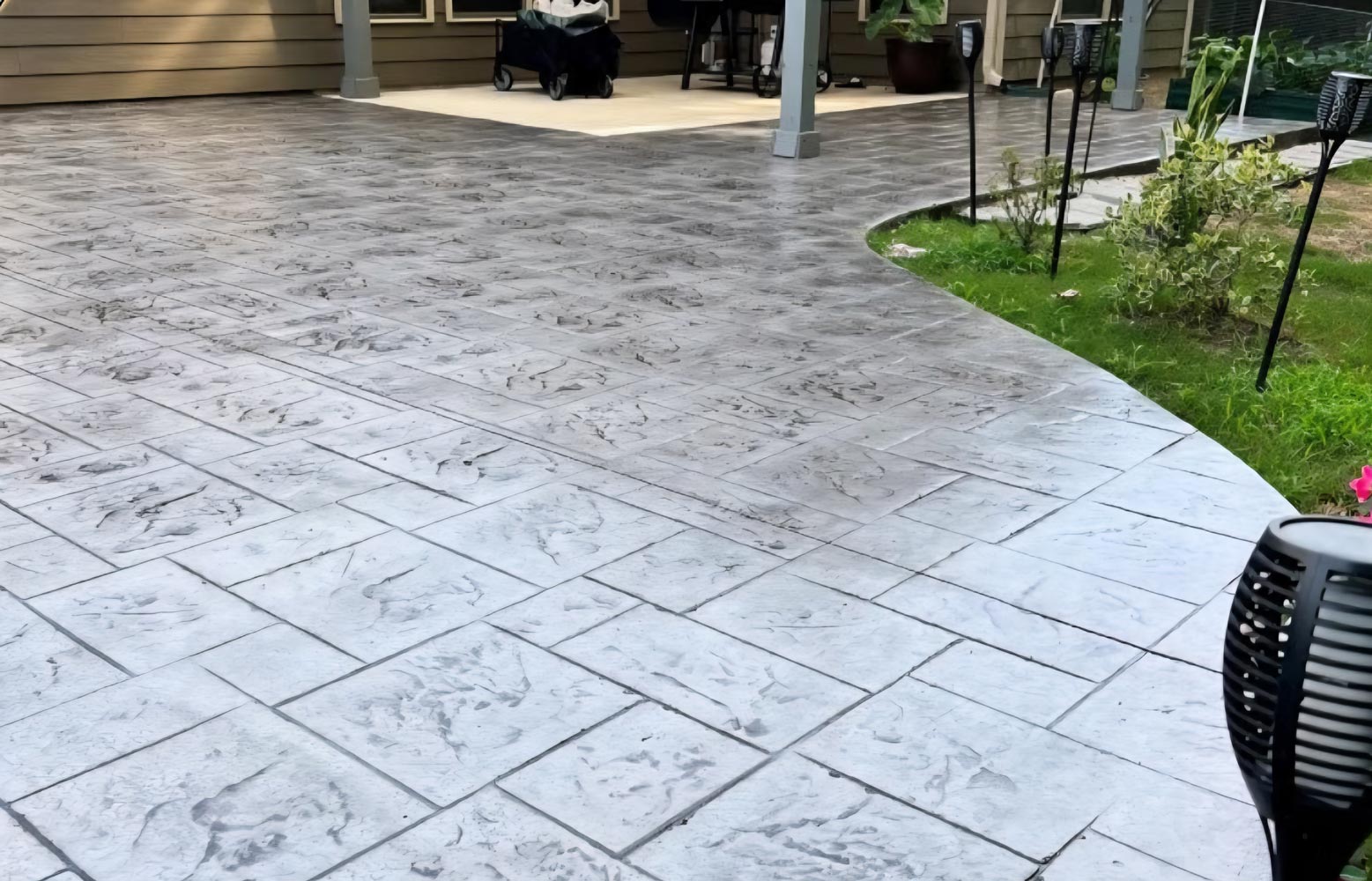 Stamped concrete patio with a tile pattern next to grass and a garden, leading to a covered porch area.